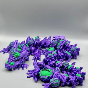 May include: A group of small, purple, 3D printed figurines with green eyes. The figurines are shaped like dragons with intricate details and textured surfaces.