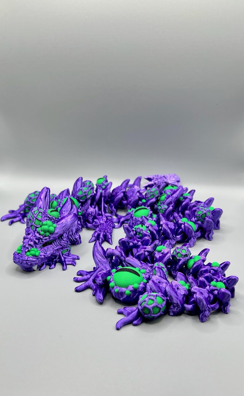 Op de afbeelding: Een groep kleine, paarse, 3D-geprinte figuurtjes met groene ogen. De figuurtjes zijn gevormd als draken met ingewikkelde details en textuur.