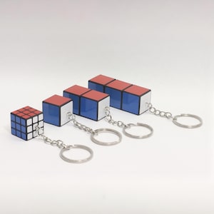Può includere: Quattro portachiavi di diverse dimensioni con un design a cubo puzzle rosso, bianco e blu. I portachiavi sono attaccati a anelli portachiavi argentati.