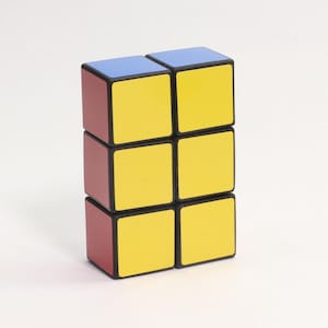 Könnte beinhalten: Ein sechs Würfel Puzzle-Spielzeug mit rechteckiger Form. Die oberen zwei Würfel sind blau, die mittleren und unteren Würfel sind gelb. Die Seiten der Würfel sind rot und die Kanten schwarz. Das Spielzeug steht auf einer weißen Oberfläche.