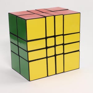 Könnte beinhalten: Ein mehrfarbiger Puzzle-Würfel mit roten, grünen und gelben Seiten. Der Würfel ist ein klassischer Denksport, bei dem jede Seite ein Raster aus kleineren Quadraten aufweist, die gedreht und neu angeordnet werden können.