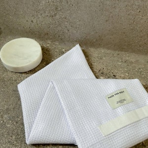 May include: White waffle weave bath towel with a white elastic strap and a white label that says "MADE FOR BODY".
