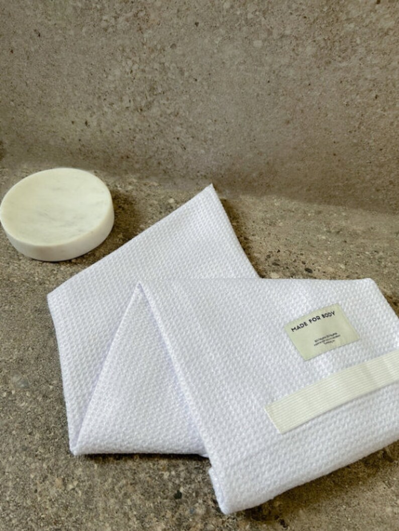 May include: White waffle weave bath towel with a white elastic strap and a white label that says "MADE FOR BODY".