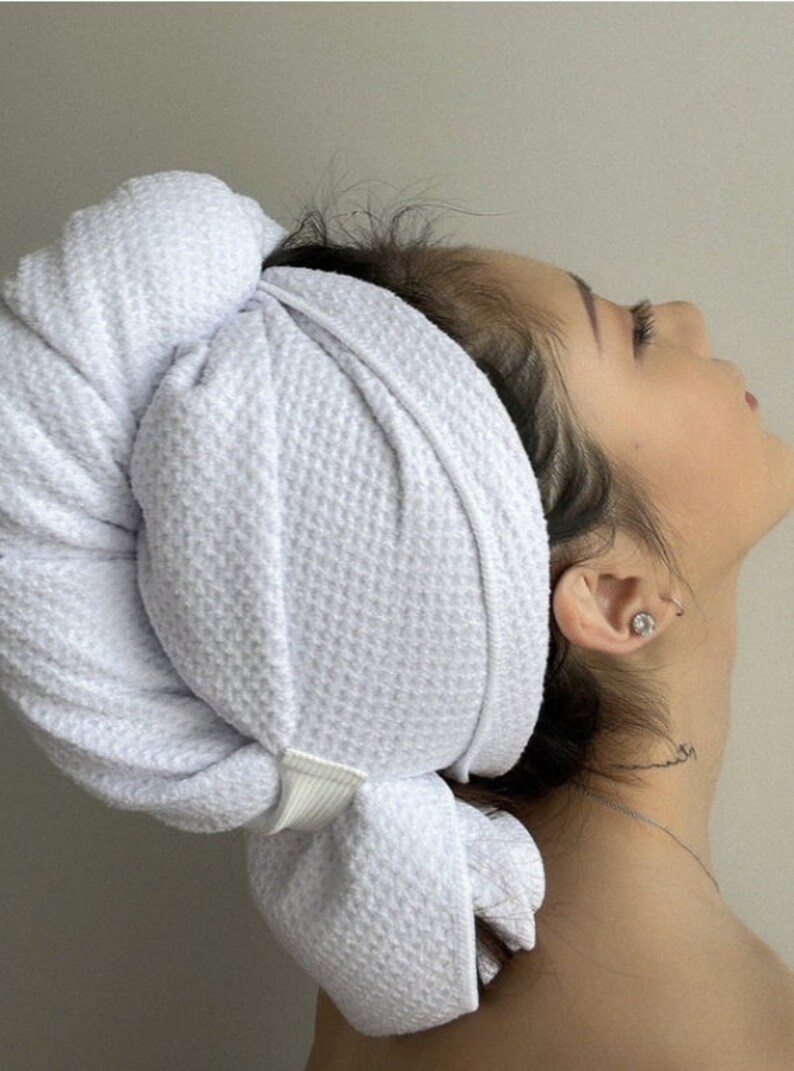 May include: A white microfiber hair towel with a white elastic band. The towel is wrapped around a person's head, with the elastic band securing it in place.