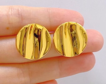 May include: A pair of gold-toned earrings with a textured, wavy design. The earrings are round and have a smooth, polished finish.