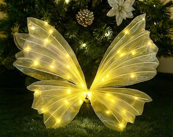 May include: A decorative light-up butterfly with a Christmas theme. The butterfly has yellow wings with embedded lights, set against a backdrop of a decorated Christmas tree. The text "Light-Up Butterfly - Decor - Christmas Edition" is at the bottom.