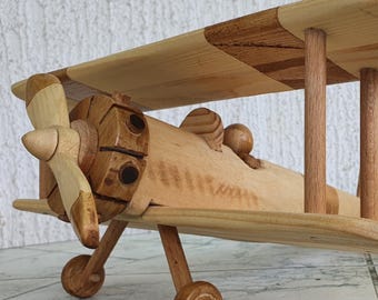 May include: A wooden toy airplane with a propeller and two wings. The airplane is made of light brown wood and has a natural wood finish.