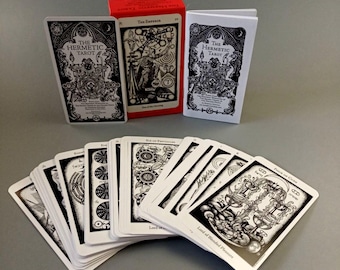 May include: A deck of The Hermetic Tarot cards, featuring black and white illustrations on white card stock. The cards are fanned out, revealing the backs of the cards, which feature a black and white design. The cards are accompanied by a red box and a small booklet, both of which feature the same black and white design as the cards.