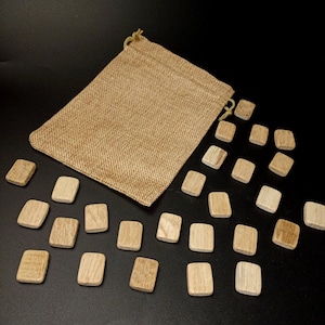 Puede incluir: Un conjunto de 25 fichas de madera en una bolsa de arpillera con cordón. Las fichas son de color marrón claro y de forma rectangular.