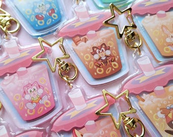 May include: A set of six colorful character-themed keychain charms featuring a pink, blue, brown, and orange drink with a white foam top. Each charm has a different character from the Sonic the Hedgehog franchise, including Sonic, Tails, Knuckles, and Shadow. The charms are made of clear acrylic and have a gold star-shaped charm attached to a gold chain.