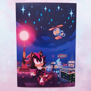 May include: A print featuring a character from the Sonic the Hedgehog series, sitting on a rooftop at night. The character is holding a can of soda. The background includes a cityscape, stars, and a flying robot. The words "Sonic Team" are visible.
