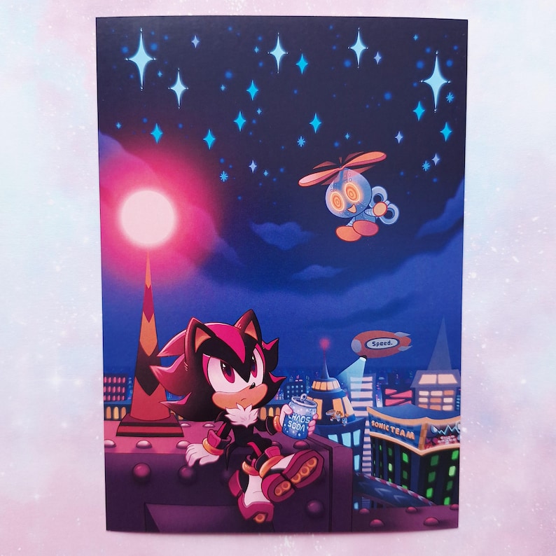 May include: A print featuring a character from the Sonic the Hedgehog series, sitting on a rooftop at night. The character is holding a can of soda. The background includes a cityscape, stars, and a flying robot. The words "Sonic Team" are visible.