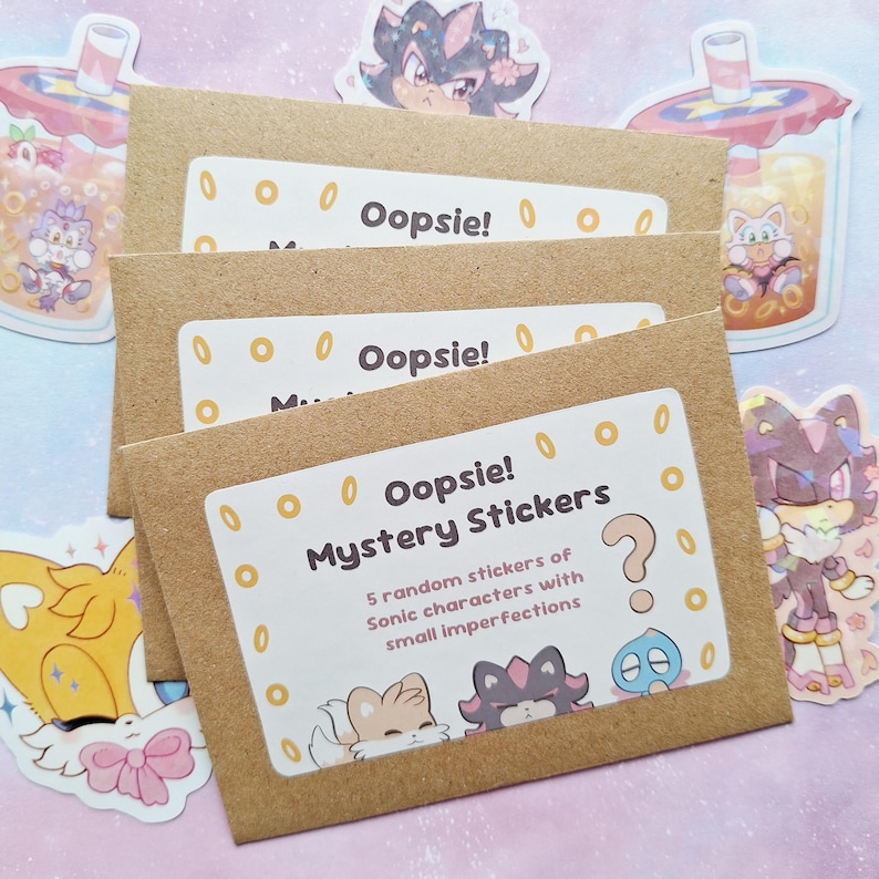 May include: Several brown paper envelopes with white labels that read "Oopsie! Mystery Stickers." The labels also state "5 random stickers of Sonic characters with small imperfections." Various Sonic character stickers are scattered around the envelopes.
