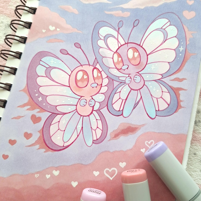 May include: A charming illustration featuring two cartoon butterflies with large eyes and pastel wings. The butterflies are pink, blue, and purple, set against a soft pink and blue background with heart shapes. Markers are visible in the foreground.