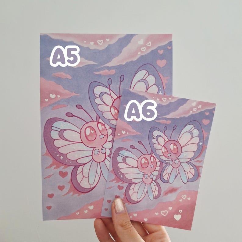 May include: Two art prints with cartoon butterflies in pink, purple, and white. The prints are labelled "A5" and "A6" in white text. The background has a sky design with hearts.