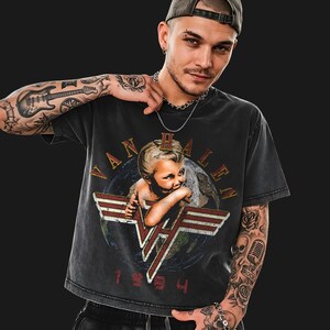 Pode incluir: Camiseta preta com um gráfico retrô de Van Halen. O design inclui o nome da banda, um anjo bebê e o ano de 1984. A camiseta tem um visual desgastado.
