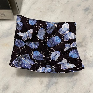 May include: A black fabric bowl with a blue and white butterfly pattern. The bowl is perfect for holding small items like jewelry or keys.