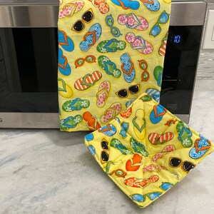 May include: A set of two yellow fabric pot holders with a pattern of flip flops and sunglasses. The pot holders are made of quilted fabric and are perfect for protecting your hands from hot dishes.