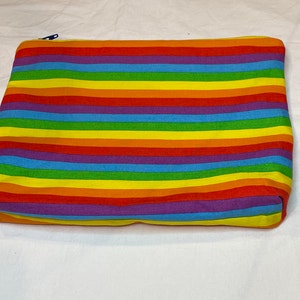 May include: A rainbow striped zippered pouch made of fabric. The pouch is a flat rectangle with a zipper across the top.