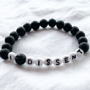 Peut inclure: Un bracelet en pierre de lave noire avec des perles blanches qui &eacute;pellent "I DISSENT".