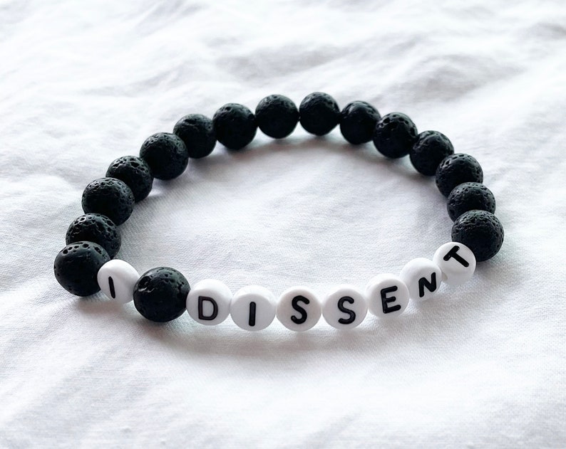 Peut inclure: Un bracelet en pierre de lave noire avec des perles blanches qui &eacute;pellent "I DISSENT".