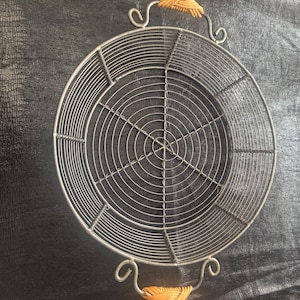 May include: A silver wire cooling rack with a woven design and two brown wooden handles.
