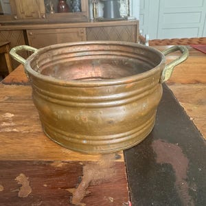 Peut inclure: Un grand pot rond en cuivre avec deux poignées en laiton. Le pot a une finition martelée et est légèrement terni.