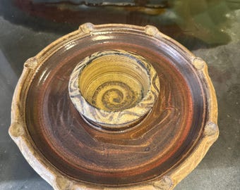 Könnte beinhalten: Ein brauner und gelber Kerzenhalter aus Keramik mit einem Spiralmuster. Der Halter hat einen erhöhten Rand und eine kleine, runde Vertiefung in der Mitte.