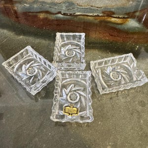 May include: Four clear crystal square dishes with a starburst design in the center. The dishes have a textured, scalloped edge. One dish has a gold and white label that reads "Crystal".