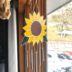 May include: A stained glass sunflower wind chime with a brown center and yellow petals. The chime has five silver tubes hanging from it.
