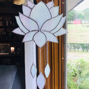 May include: A white stained glass lotus flower with iridescent accents hangs from a silver chain with three dangling white stained glass leaves.