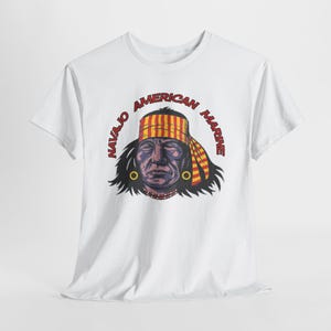 May include: White t-shirt featuring a graphic of a Native American man with the text "NAVAJO AMERICAN MARINE" in a red arc around the image. The man is depicted with a colorful headdress and earrings.