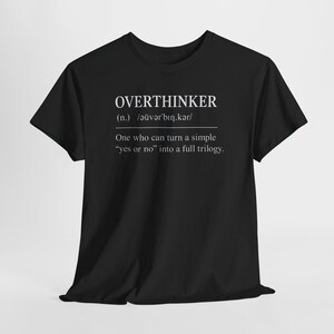 以下が含まれることがあります： 黒いTシャツ。白で「OVERTHINKER」の文字、発音記号、定義が書かれています。定義は「単純な「はい」か「いいえ」を完全な三部作に変えることができる人」です。