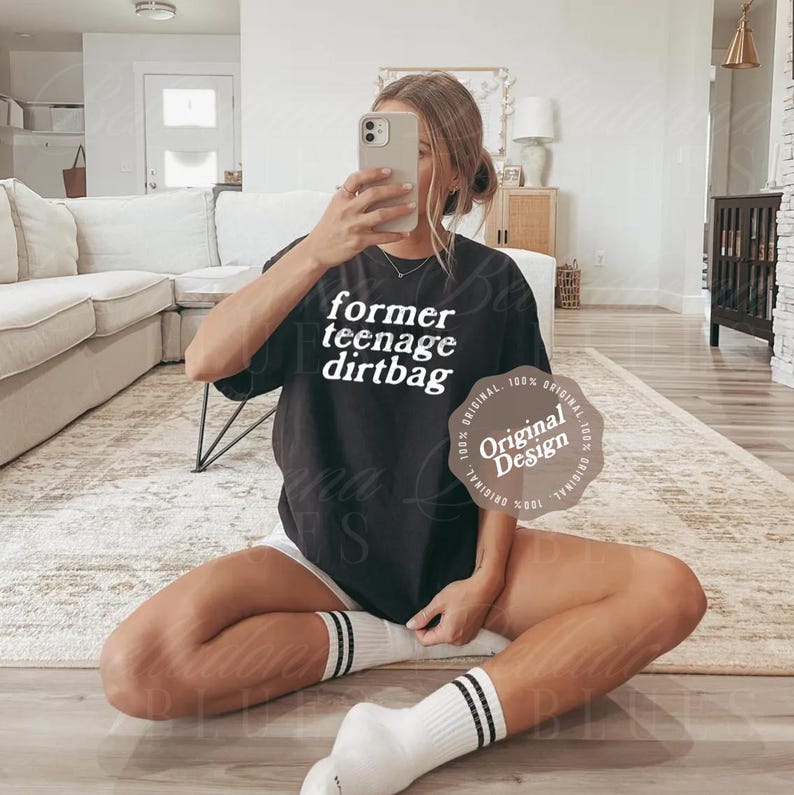 May include: A black short-sleeved t-shirt featuring the white text "former teenage dirtbag" printed on the front. The shirt has a crew neckline and a relaxed fit. A circular beige graphic with the text "Original Design" is overlaid on the right.