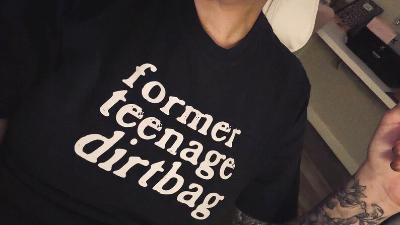 May include: A black short-sleeved t-shirt featuring the white text "former teenage dirtbag" printed in a distressed, serif font across the chest. The shirt has a classic crew neckline and a standard fit, showcasing a bold graphic design.