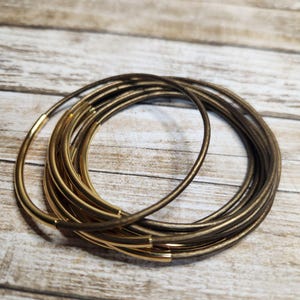 May include: A set of brown leather bracelets with gold accents. The bracelets are stacked on top of each other and are arranged in a circle.