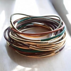 May include: A stack of gold and leather bracelets with green, brown, and purple accents.