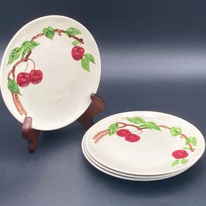 May include: A white ceramic mug with a black handle and the text "But First, Coffee" in a bold, black font. The mug is set against a blurred background, suggesting a cozy setting.