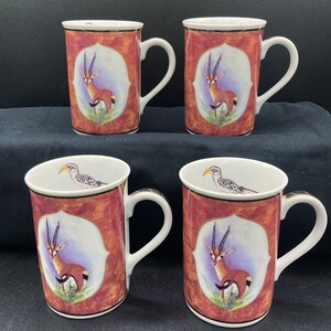 May include: Set of four white ceramic mugs with red and gold accents. Each mug features a different animal illustration: a bird, a gazelle, and a gazelle in a frame.