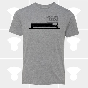 May include: A heather gray t-shirt with a black graphic of a stereo component and the text "DROP THE NEEDLE" above it. The shirt has short sleeves and a crew neck.