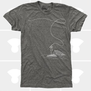 May include: Heather gray t-shirt featuring a white line drawing of a person fly fishing. The illustration shows the person standing on a rock in the water, casting a line. The shirt has a crew neck and short sleeves.