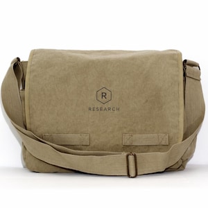 May include: A tan messenger bag with a shoulder strap. The bag has a flap closure and a buckle. The word "RESEARCH" is printed below a hexagon with the letter "R" inside.