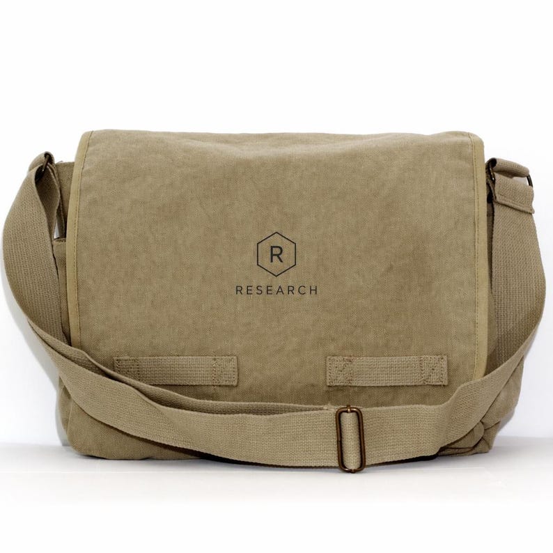 May include: A tan messenger bag with a shoulder strap. The bag has a flap closure and a buckle. The word "RESEARCH" is printed below a hexagon with the letter "R" inside.