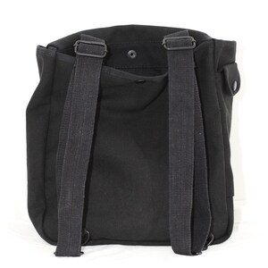 May include: Black canvas backpack with adjustable shoulder straps and a top flap closure. The bag features a small pocket on the side and a snap closure. The straps are made of a durable, woven material. The backpack is designed for carrying items.