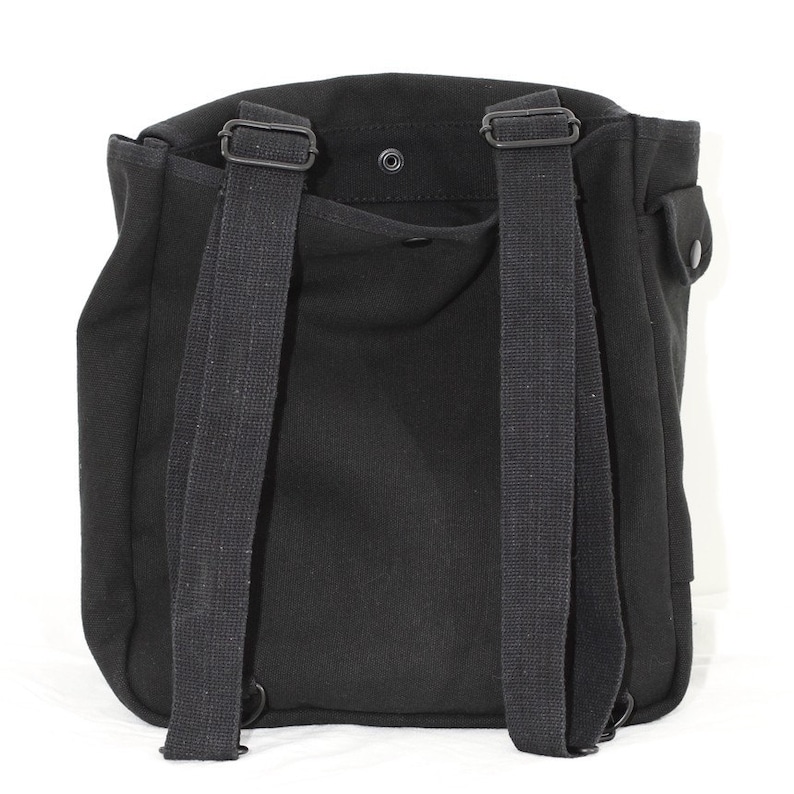 May include: Black canvas backpack with adjustable shoulder straps and a top flap closure. The bag features a small pocket on the side and a snap closure. The straps are made of a durable, woven material. The backpack is designed for carrying items.