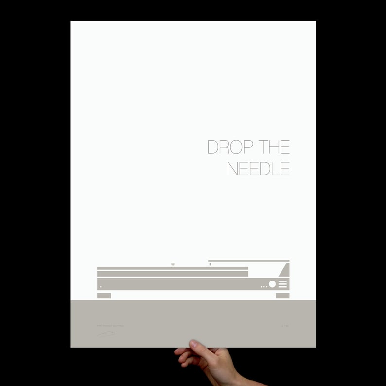 May include: A minimalist poster featuring a gray illustration of a record player with the text "DROP THE NEEDLE" in a light gray font. The poster is held by a hand against a black background.