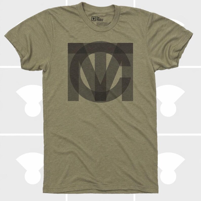 Pu&ograve; includere: T-shirt verde oliva con un design geometrico grigio scuro al centro. Il design presenta lettere sovrapposte, forse un'iniziale o un logo. La maglietta ha maniche corte e girocollo.