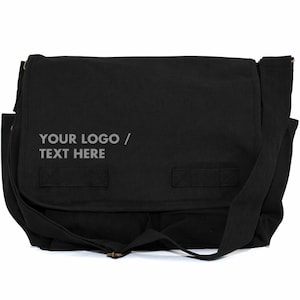 May include: Black messenger bag with a flap closure and adjustable shoulder strap. The bag features the text "YOUR LOGO / TEXT HERE" in a light grey colour. The bag has two small straps on the front.