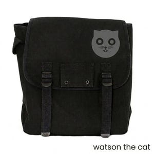 May include: Black canvas messenger bag with a flap closure, adjustable straps, and a gray cat face graphic. The text "watson the cat" is printed at the bottom. This bag is suitable for carrying books, laptops, or other essentials.