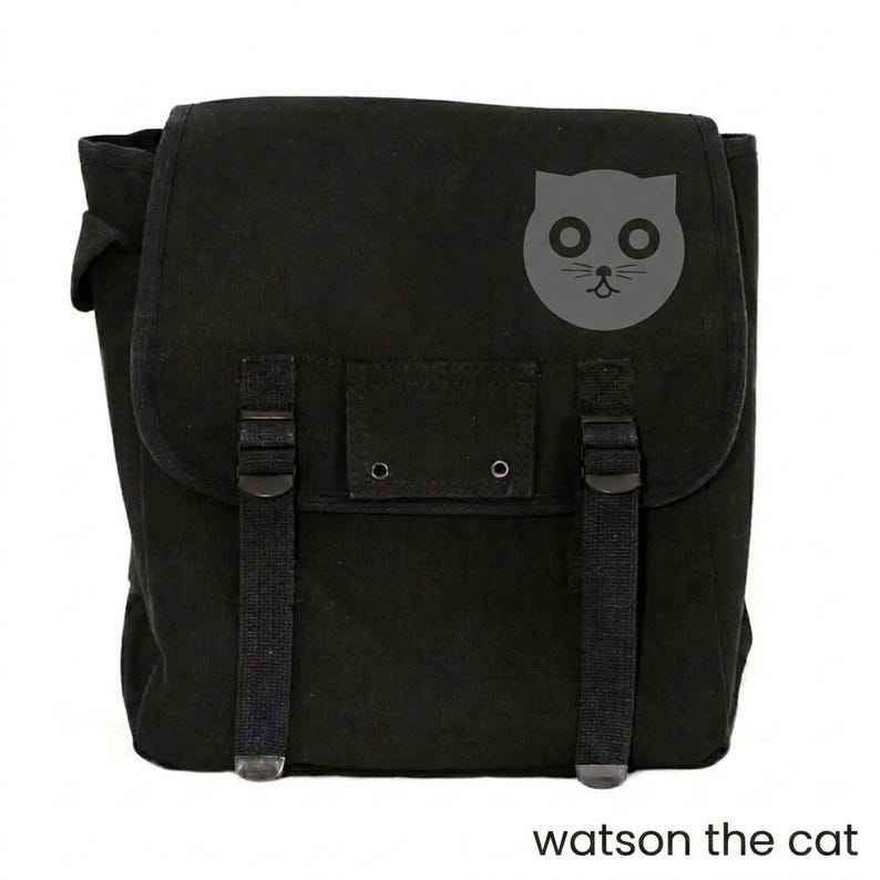 May include: Black canvas messenger bag with a flap closure, adjustable straps, and a gray cat face graphic. The text "watson the cat" is printed at the bottom. This bag is suitable for carrying books, laptops, or other essentials.
